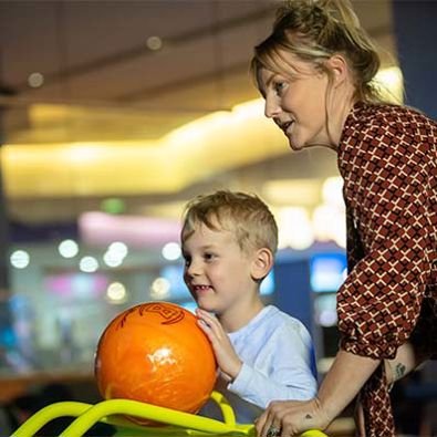 Mother and son pushing orange bowling ball down a ramp