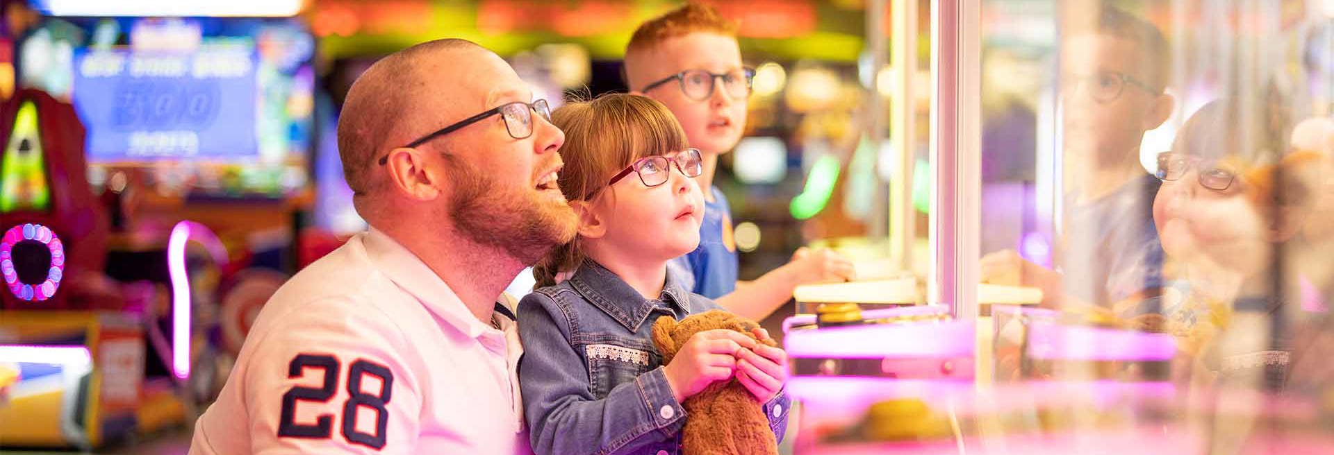 father and daughter playing on a crane amusement arcade with son in the background at namco funscape metrocentre