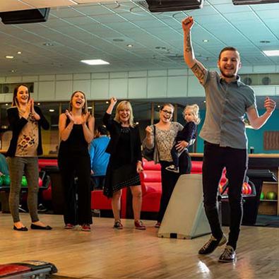 Group of friends cheering whilst playing a game of bowling