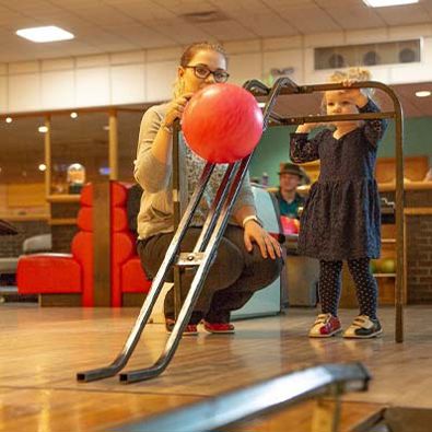 Mother and daughter pushing a red bowling bowl down a ramp