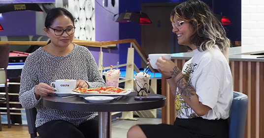 Two women enjoying pizza, coffee and milkshakes