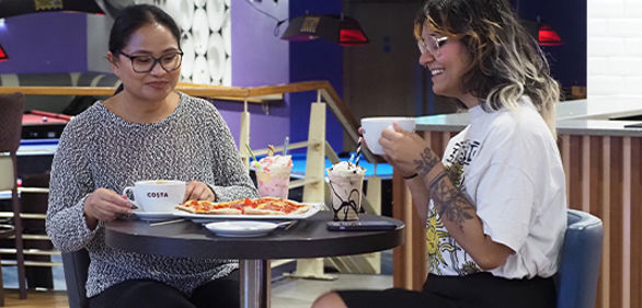 Two women enjoying pizza, coffee and milkshakes