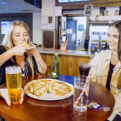 Two woman at the bar enjoying a pizza and alcoholic beverages 