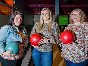 Group of women holding bowling balls and smiling cheerfully 