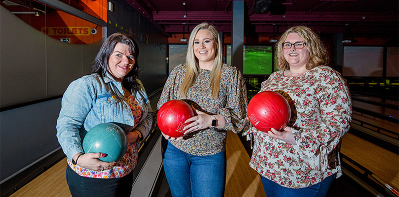 Group of women holding bowling balls and smiling cheerfully 