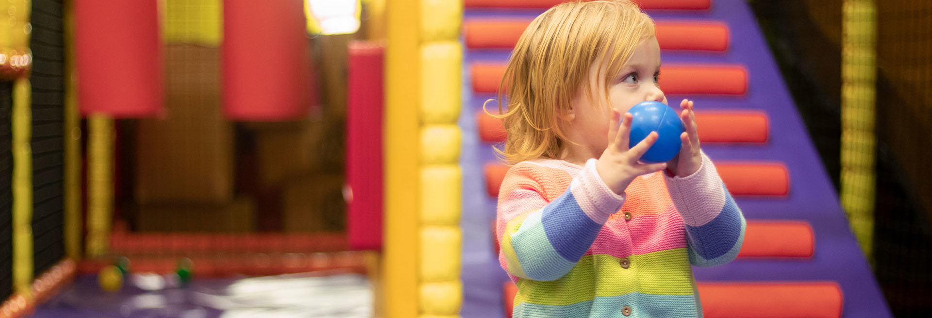 Young girl holding a blue ball and playing in soft play at namco funscape