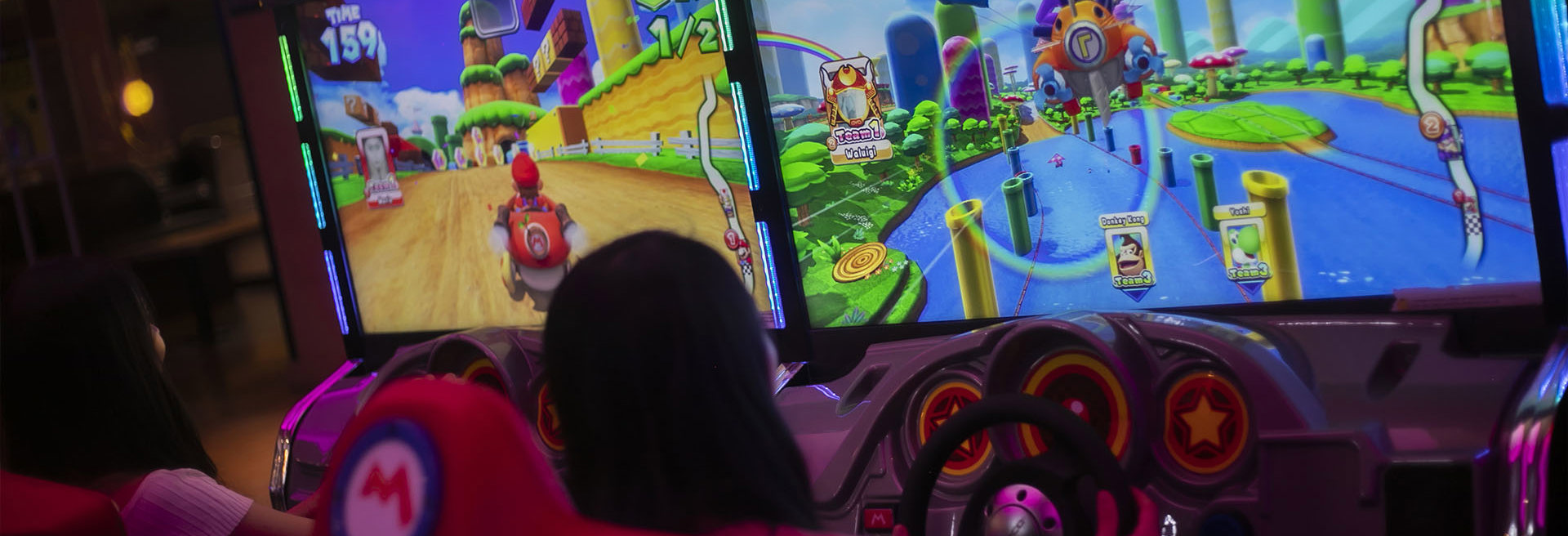 Two girls playing mario cart driving arcade game at namco funscape