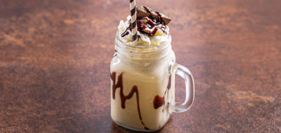 A mint chocolate milkshake in a jar mug, topped with a swirl of whipped cream, chocolate shavings, and mint chocolate