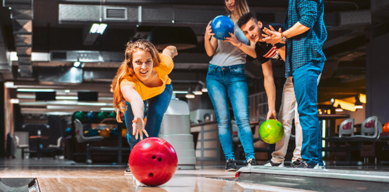 girl bowling with a red ball whilst friends look on and cheer