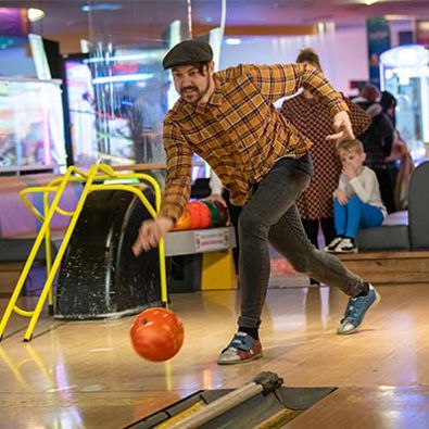 Male throwing an orange bowling ball down a bowling lane