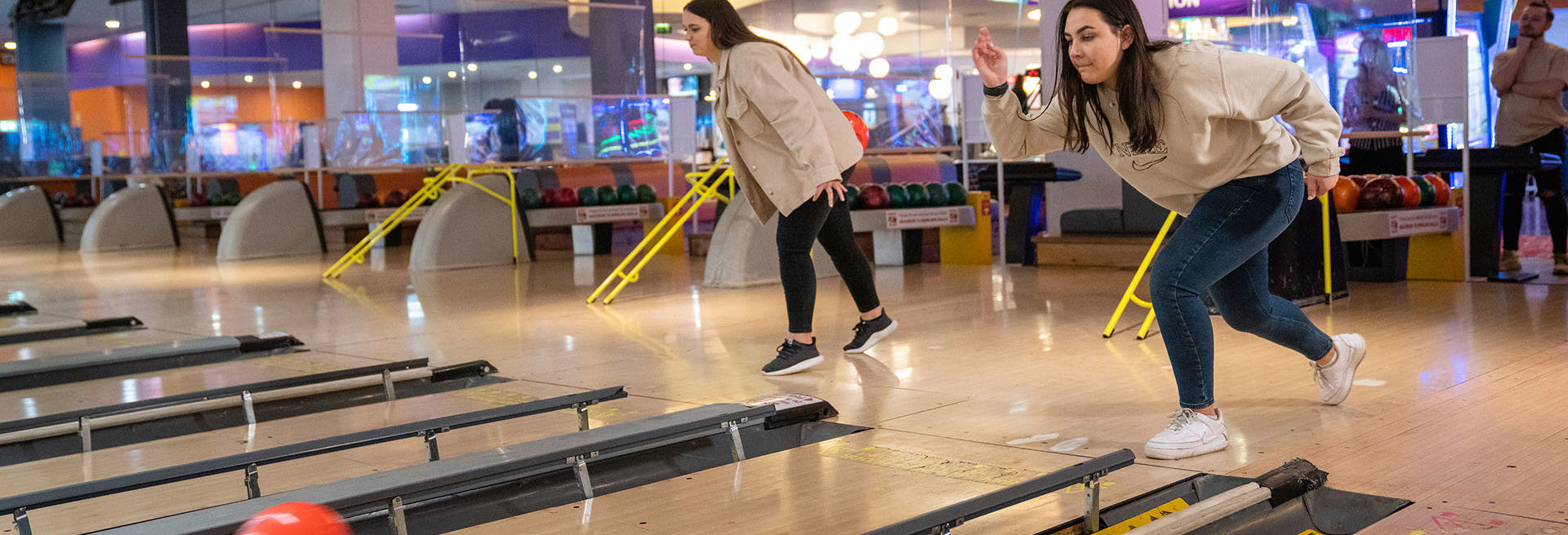 Two girls rolling bowling ball down a polished bowling lane
