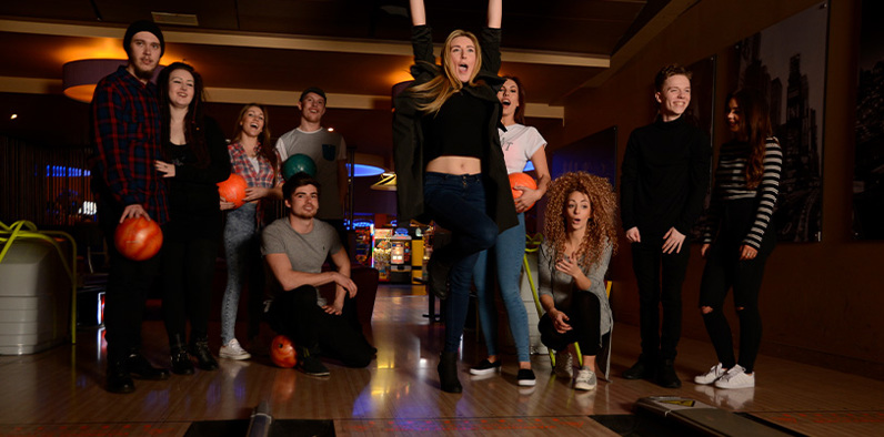 Group of friends cheering whilst playing a game of bowling