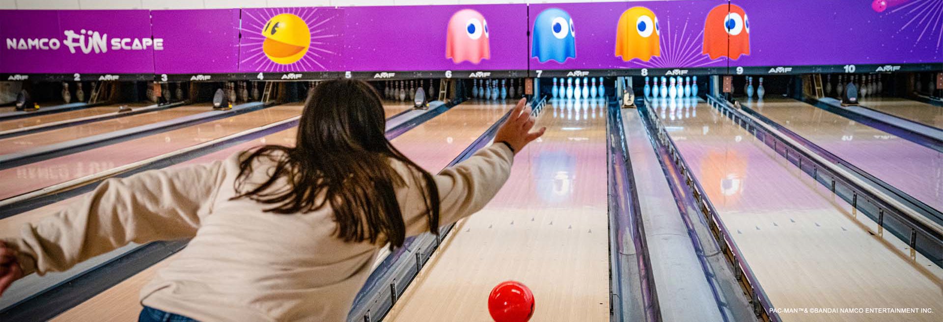 Woman throwing a red bowling bowl down a bowling lane at namco funscape
