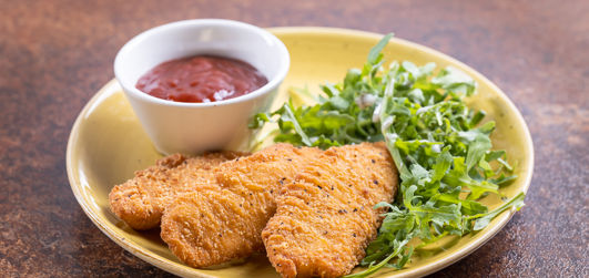 Chicken pieces served on a plate with ketchup and salad