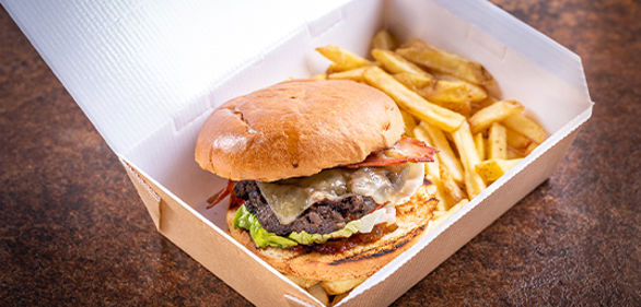 Beef burger with bacon and chips in a takeaway box