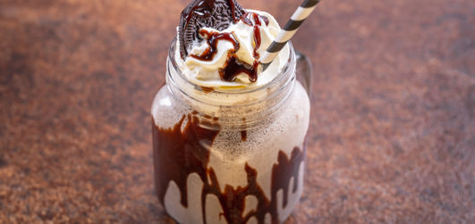 A delicious Oreo milkshake in a glass jar, topped with whipped cream and crumbled Oreo cookies, served with a striped straw.