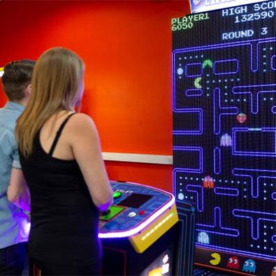 Girl and boy immersed in a Pac-Man arcade game as they navigate the iconic maze, avoiding ghosts and collecting dots together