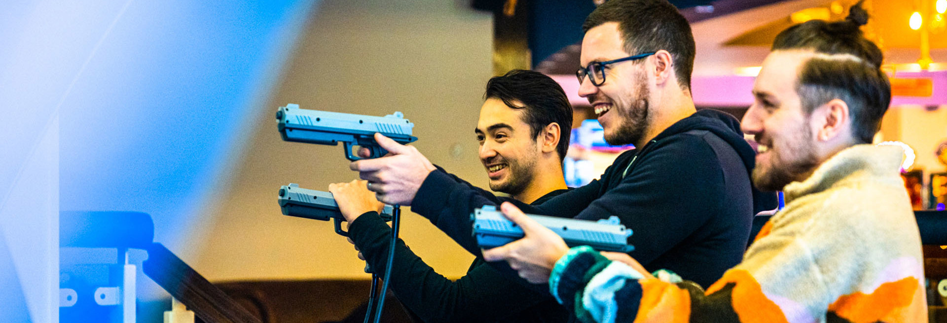 Group of men laughing and playing shooting amusement arcade at namco funscape